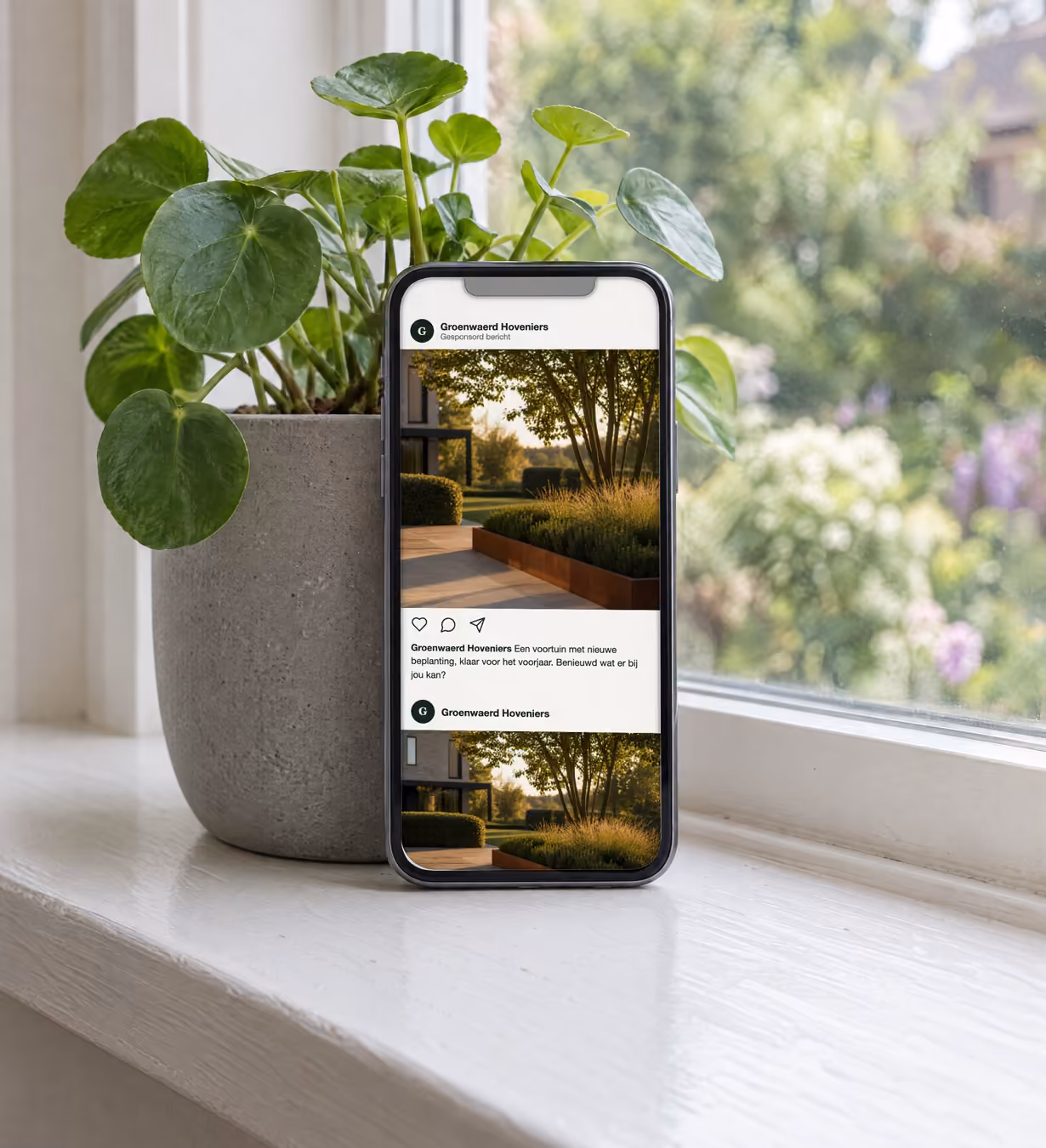 Telefoon rechtop tegen een plantenpot op een vensterbank. Op het scherm een voorbeeld van een social-mediapagina voor een fictief hoveniersbedrijf, met een bericht van de hovenier met een foto van een voortuin